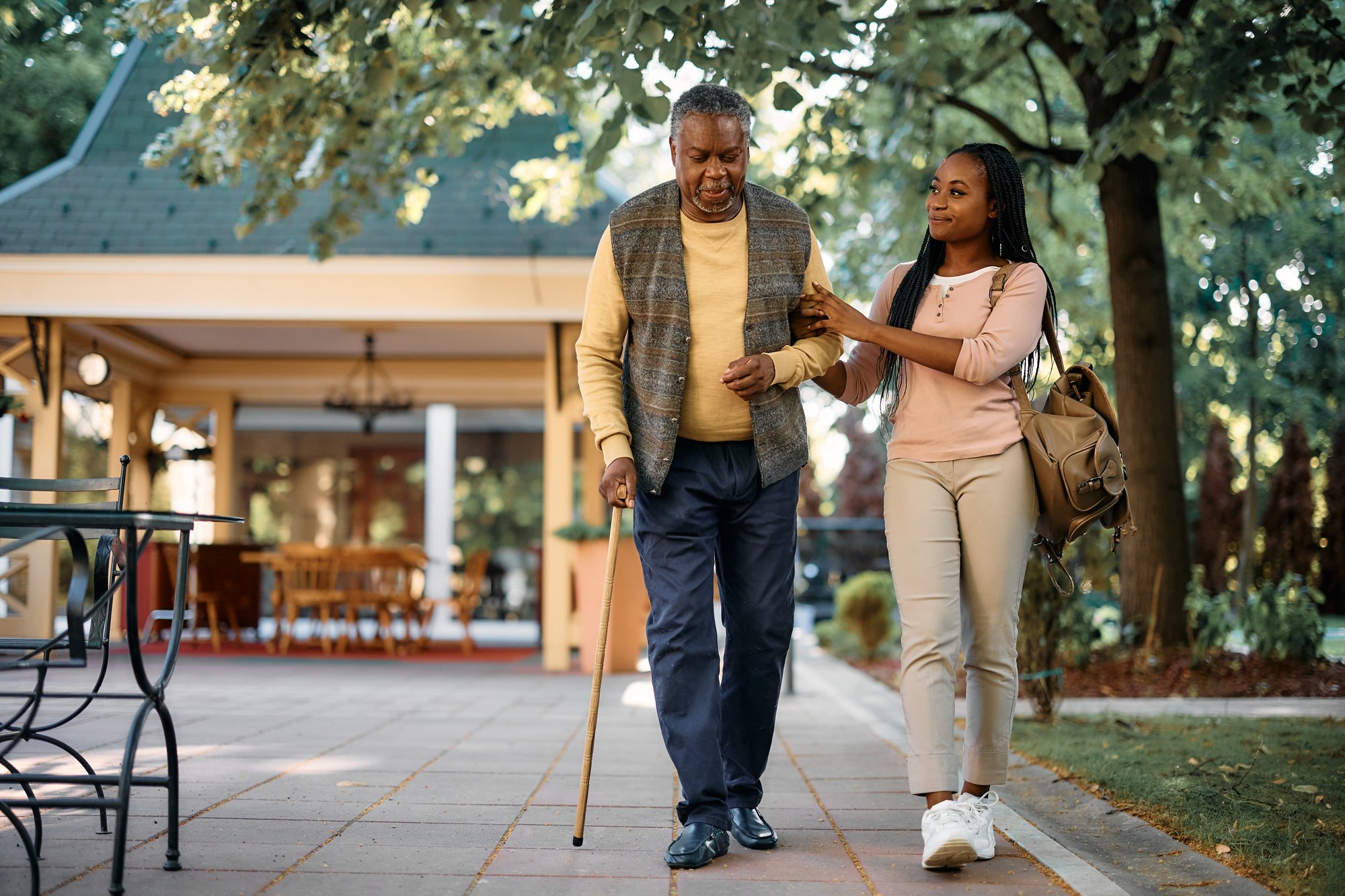 Older man walking with a cane and his daughter outdoors Older man walking with a cane and his daughter outdoors